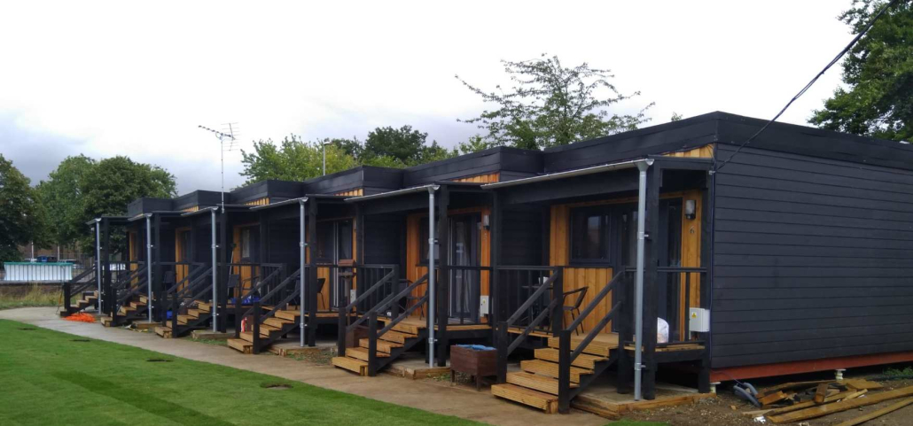 Row of modular homes made of wood and metal, steps running up to each and green lawn in front